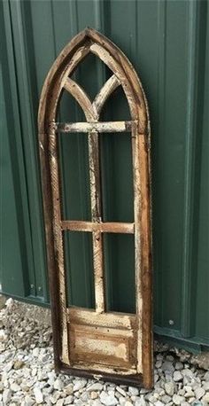 an old wooden window sitting on top of a gravel ground next to a green wall