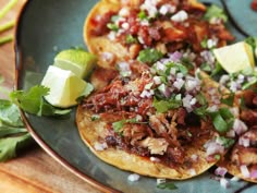 two tacos with meat, onions and cilantro on a plate next to lime wedges