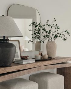 a wooden table topped with a mirror and vase filled with flowers next to two stools