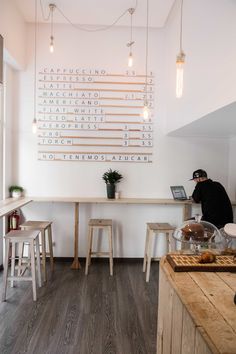 a person standing at a counter in a room with wooden stools and lights hanging from the ceiling