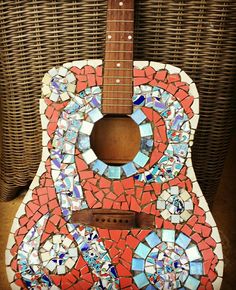 an acoustic guitar made out of mosaic tiles and glass beads, sitting on a wicker chair