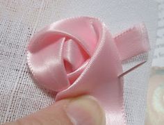 a hand is holding a pink ribbon on a piece of fabric that has been stitched together