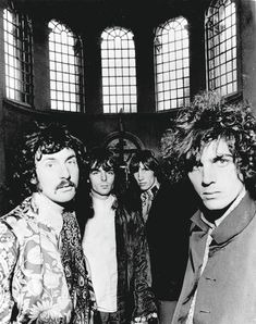 an old black and white photo of four men with long hair standing in front of three windows