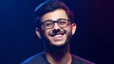 a smiling man with glasses and beard in front of a dark background smiles at the camera