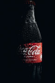 a bottle of coca cola sitting on top of a black table with water droplets all over it