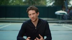 a man sitting on top of a tennis court holding his hands out in front of him