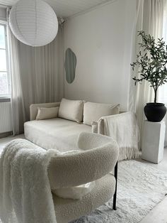 a living room with a white couch, chair and potted plant in the corner