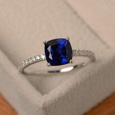 an engagement ring with a blue cushion cut sapphire surrounded by white diamonds in a box