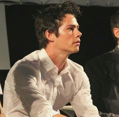 two men sitting next to each other in front of a microphone and one man wearing a white shirt