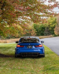 a blue car parked on the side of a road next to a tree with red leaves