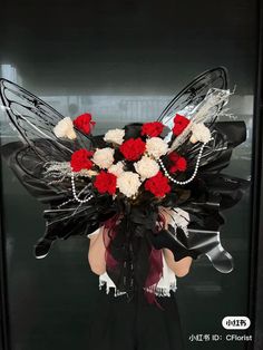 a woman holding a bouquet of red and white flowers in front of a black door