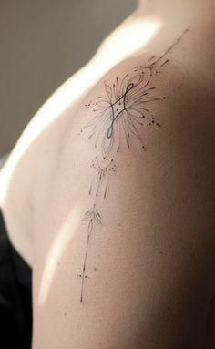 the back of a woman's shoulder with a dandelion tattoo on it