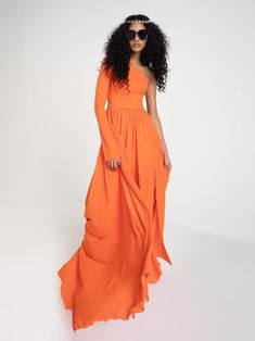 a woman in an orange dress with sunglasses on her head and long curly hair standing against a white background