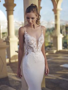 a woman in a white wedding dress standing on a stone walkway with columns and arches