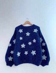 a blue sweater with white stars is hanging on a hanger against a white wall