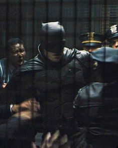 the dark knight rises behind bars in a caged area with other people looking on