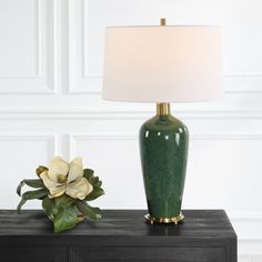 a green vase sitting on top of a black table next to a white lamp shade