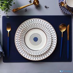 a place setting with blue and white plates, silverware and gold utensils