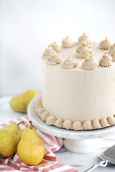 a white cake sitting on top of a table next to two pears