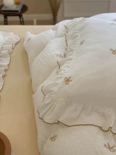 a bed with white linens and gold embroidered trim on the pillow cases, along with a pair of flip flops