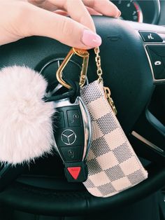 a hand holding a car key chain with a fur ball hanging from it's center console