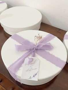 three white boxes with purple ribbons and tags on them sitting on a table next to each other