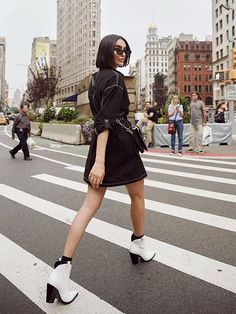 a woman crossing the street wearing high heeled shoes and a black dress with white trim