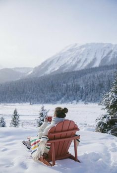 a woman sitting in a red chair on top of a snow covered slope next to trees