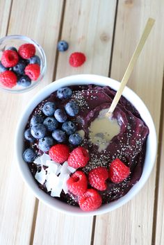 a bowl filled with blueberries and raspberries next to a glass of yogurt