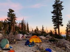 there are many tents set up on the rocky hill side with trees in the background