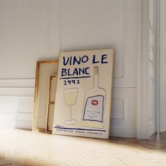 a wine bottle and glass are sitting on the floor next to a framed sign that reads vino le blanc