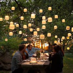 a group of people sitting around a table with paper lantern lights hanging from the ceiling