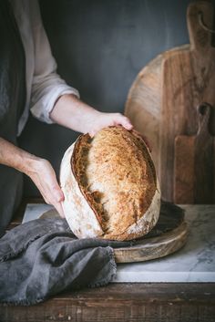 a person holding a loaf of bread on top of a cutting board