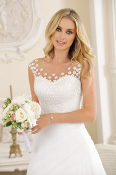 a woman in a white wedding dress holding a bridal bouquet and looking at the camera