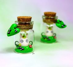 two small glass jars with animals in them on a white surface, one has a cork top and the other is green