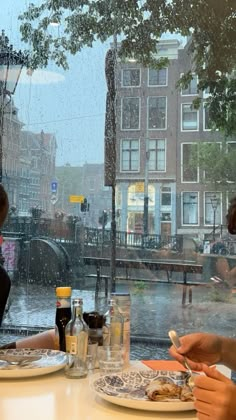 two people sitting at a table with plates of food in front of them, looking out the window