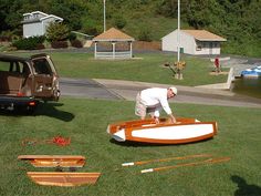 a man working on a wooden boat in the grass next to other boats and vehicles