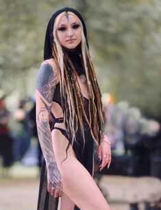 a woman with dreadlocks is standing on a skateboard in the park and has tattoos on her body