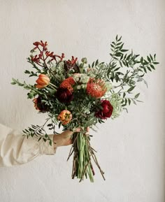 a person holding a bouquet of flowers in their hand with greenery on the side