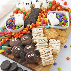 an assortment of halloween treats on a cutting board with candy and candies in the background