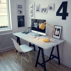 a desk with a computer on it in front of a window and pictures hanging on the wall