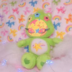 a green teddy bear sitting on top of a bed covered in white fluffy blankets and rainbows