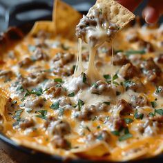 a person holding a tortilla chip with meat and cheese on it in a skillet