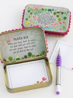 two tins with writing on them next to a pen and paper in the box