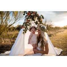 a woman sitting on the ground holding a baby in her arms and wearing a flower crown