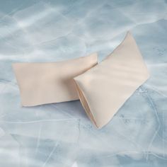 two white pillows laying next to each other on top of a blue tablecloth covered surface