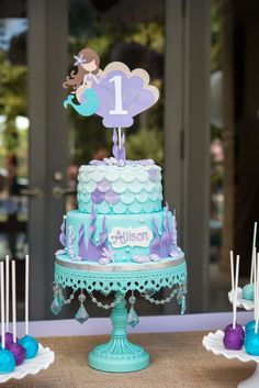 a little mermaid birthday cake on a table with lollipops and marshmallows