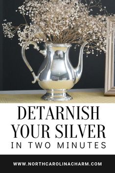 a silver pitcher filled with white flowers on top of a table next to a framed photo