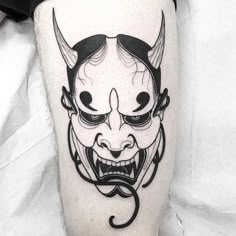 a black and white photo of a demon tattoo on the leg with an evil face