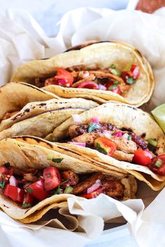 three tacos with meat, tomatoes and lettuce on paper in a basket